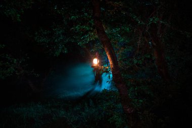 Korku Cadılar Bayramı konsepti. Geceleri ormanda eski yağ lambası yakmak. Kabus sahnesinin gece manzarası.