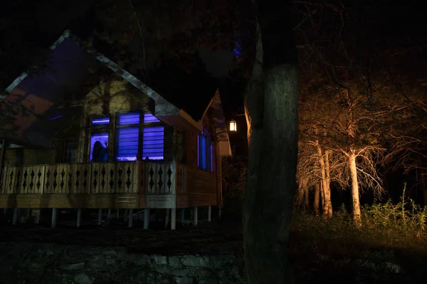 Gammalt hus med en Ghost i skogen på natten eller Övergiven Haunted Horror House i dimma. Gammal mystisk byggnad i död trädskog. Träd på natten med månen. Surrealistiska ljus. Halloween-konceptet — Stockfoto