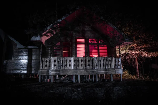 Casa velha com um fantasma na floresta à noite ou Abandonada Haunted Horror House no nevoeiro. Um velho edifício místico numa floresta de árvores mortas. Árvores à noite com lua. Luzes surreais. Conceito de Halloween horrível — Fotografia de Stock