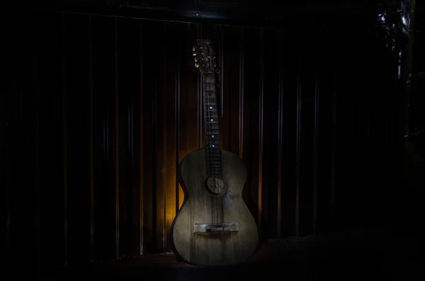 An wooden acoustic guitar is against a grunge textured wall. The room is dark with a spotlight for your copyspace.