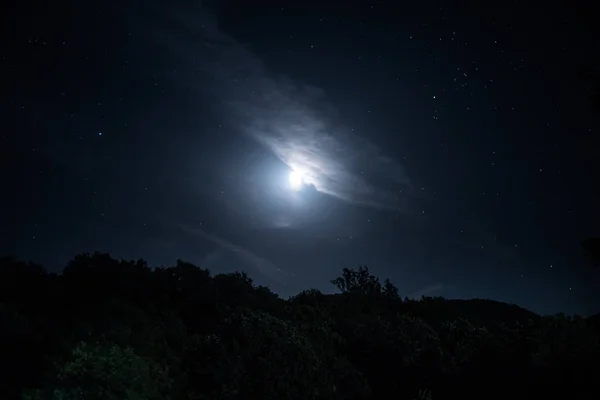 Горная дорога через лес в полнолуние. Сценический ночной пейзаж темно-синего неба с луной. — стоковое фото