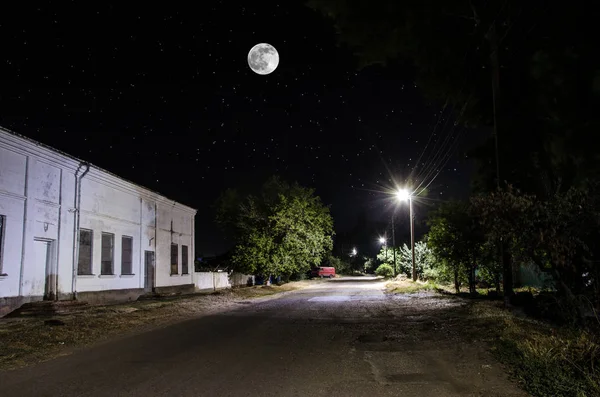 Luna llena sobre un pueblo tranquilo por la noche. Hermoso paisaje nocturno de la calle del casco antiguo con luces. Rusia — Foto de Stock