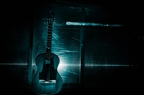 Eine hölzerne Akustikgitarre steht vor einer grunge-strukturierten Wand. der Raum ist dunkel mit einem Scheinwerfer für Ihren Copyspace. — Stockfoto