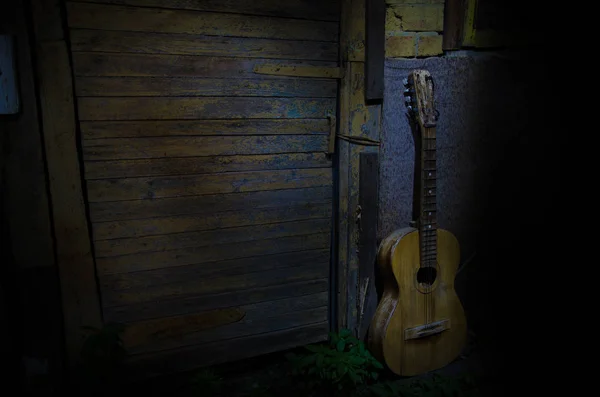 一把木制的原声吉他靠在一面有纹理的墙壁上。房间很暗,有聚光灯,适合您的复制空间. — 图库照片