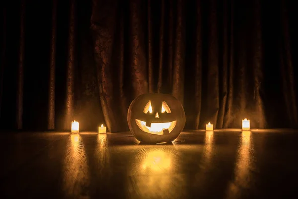 Halloween pumpkin head jack o lantern with glowing candles on background. Pumpkins on wooden floor