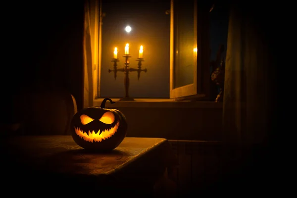 Enge Halloween pompoen in het venster van de mystieke huis bij nacht of halloween pompoen in nacht op kamer met blauwe venster. Symbool van halloween in venster. — Stockfoto