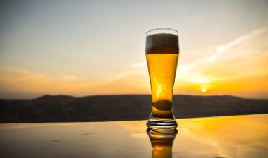Gün batımında sahilde bir bardak bira. Soğutma yaz içki konsepti. Güneş ışığı Arka Plan Bokeh ile Draught Bira Bir Bardak Close Up