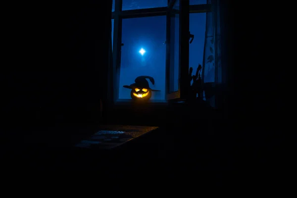 Scary Halloween pumpkin in the mystical house window at night or halloween pumpkin in night on room with blue window. Symbol of halloween in window.