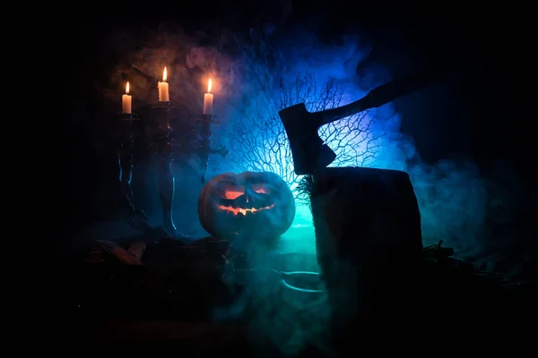 Zucca arancione spaventosa con occhi scolpiti e un sorriso con candele accese e un'ascia — Foto Stock