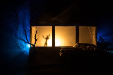 Geceleri ormanda hayaletli eski bir ev. Pencerede korku silueti. Ormandaki eski bina. Gerçeküstü ışıklar. Korku Halloween kavramı
