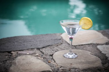 Okyanus ve palmiye ağacı arka plan ile yüzme havuzunda martini kokteyl cam. Bir bardak mavi martini kokteylhoş geldin içki barı. Seçici odak. sezon ve tatil konsepti.
