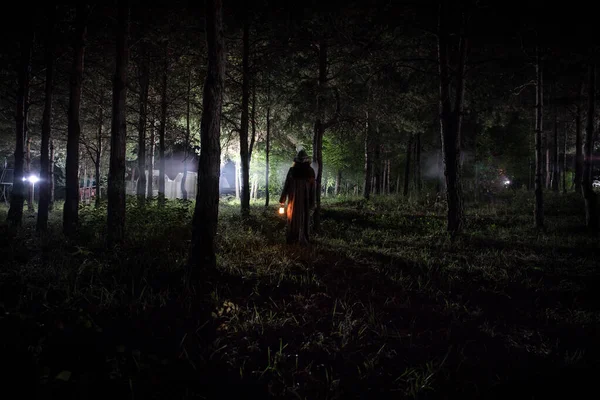 Extraña luz en un bosque oscuro por la noche. Silueta de persona de pie en el bosque oscuro con luz. Noche oscura en el bosque a la hora de niebla. Surrealista escena del bosque nocturno . — Foto de Stock