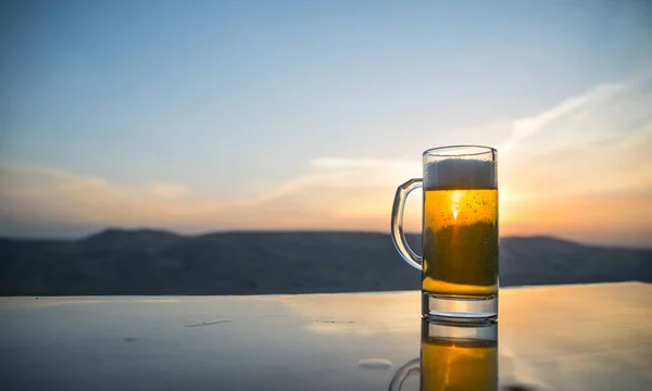 Bicchiere di birra su una spiaggia al tramonto. Raffreddamento concetto di bevanda estiva. Close Up di un bicchiere di birra alla spina con il Bokeh di sfondo luce solare — Foto Stock
