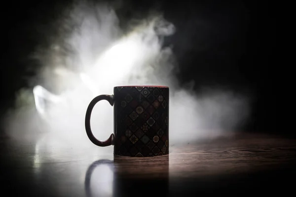 Beautiful eastern style textured ceramic cup of coffee (or tea) with smoke over dark toned background.