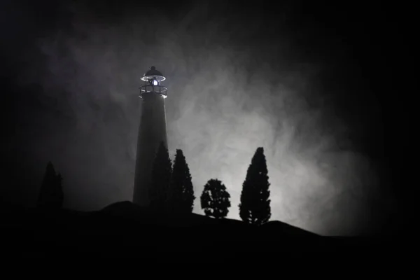 Lighthouse with light beam at night with fog. Old lighthouse standing on mountain. Table decoration. Toned background. Moonlighting.