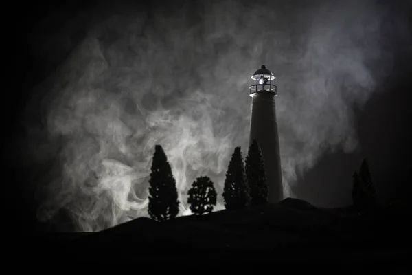 Lighthouse with light beam at night with fog. Old lighthouse standing on mountain. Table decoration. Toned background. Moonlighting.