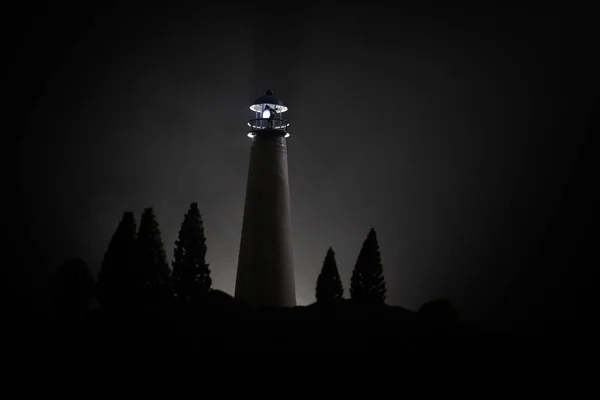 Lighthouse with light beam at night with fog. Old lighthouse standing on mountain. Table decoration. Toned background. Moonlighting.