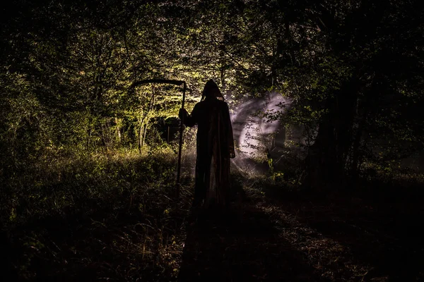 Morte con falce nell'oscura foresta nebbiosa. Donna fantasma horror che tiene il mietitore nella foresta — Foto Stock