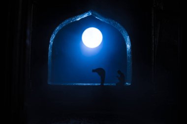 Pencere ve sütunları olan gerçekçi bir Arap iç mimarisi. Müslüman silueti pencerenin yanındaki halıda dua ediyor. Kutlama kartı, Müslüman kutsal ayı için davetiye Ramazan Kareem. Seçici odak