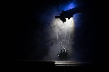 Koronavirüsle yaratıcı manipülasyon kavramı. El, manipülasyon için ipleri tutuyor. Covid19 minyatürünü kontrol eden el sisli bir arka planda sicimler taşıyor. Seçici odak