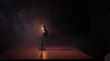 Ses, müzik için mikrofon, ses stüdyosunda ya da sahnede karaoke. Mikrofon teknolojisi. Konuşma yayın ekipmanı. Karanlık odadaki mikrofon, arka farlı masanın üstünde. Seçici odak