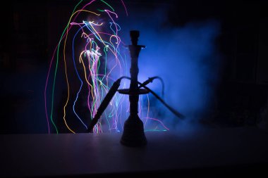 Shisha kasesinde sıcak nargile kömürleri karanlık odada buhar bulutları oluşturuyor. Karanlıkta ışık saçan şık bir oryantal shisha. Seçici odak