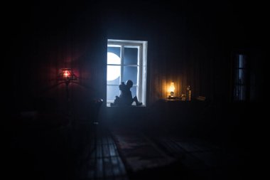 Geceleri mobilyası ve penceresi olan gerçekçi bir bebek evi oturma odası. Pencerede oturan romantik bir çift. El yapımı gerçekçi bebek eviyle sanat masası dekorasyonu. Seçici odak.