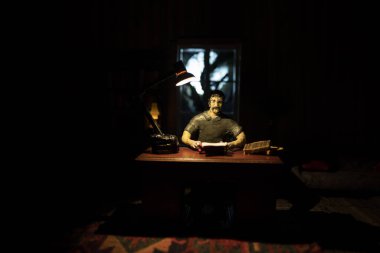 Geceleri mobilyası ve penceresi olan gerçekçi bir bebek evi oturma odası. Karanlık odada masada oturan bir adam. Küresel virüs salgını sırasında evde kalma kavramı. Seçici odak.