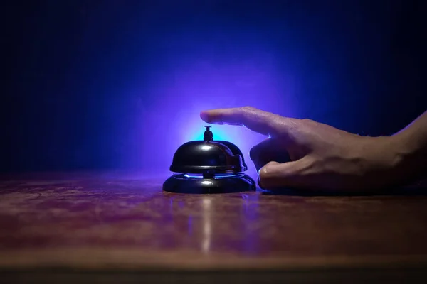 Calling service bell on wooden table with toned lights on dark background. Hotel reception bell, Hand ringing in service bell , selective focus