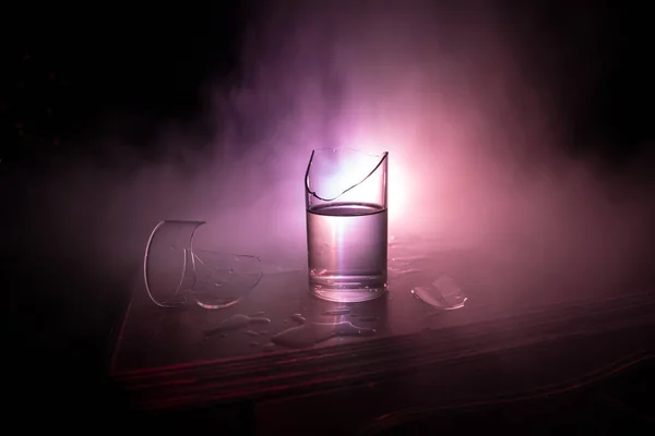 Drink, broken glass concept. Broken glasses on wooden table at dark toned background with fog. Selective focus