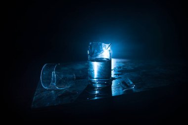 İçki, kırık cam konsepti. Ahşap masada kırık bardaklar, sisli, koyu tonlu arka plan. Seçici odak