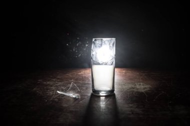 İçki, kırık cam konsepti. Ahşap masada kırık bardaklar, sisli, koyu tonlu arka plan. Seçici odak