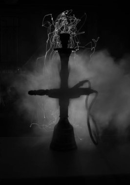 Shisha kasesinde sıcak nargile kömürleri karanlık odada buhar bulutları oluşturuyor. Karanlıkta ışık saçan şık bir oryantal shisha. Seçici odak