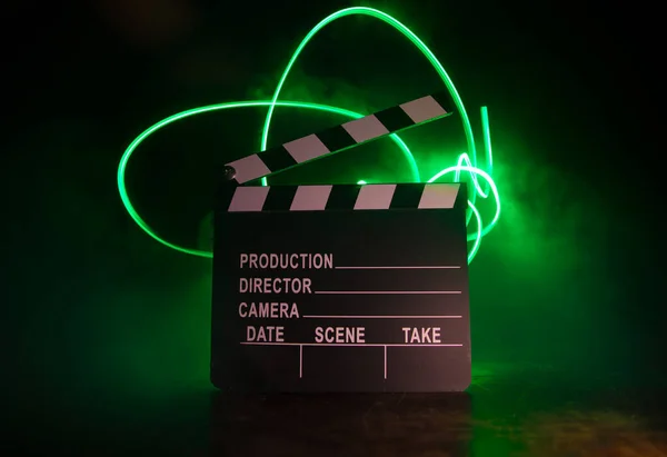 Movie concept. Miniature movie set on dark toned background with fog and empty space. Silhouette of clapboard on dark. Selective focus