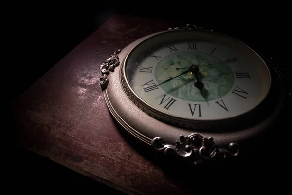 Time concept. Big vintage round clock on wooden table with abstract light. Dark atmosphere. Creative decoration. Selective focus