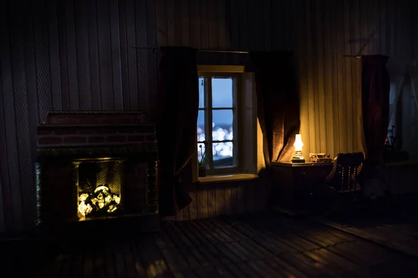 A realistic dollhouse living room with furniture and window at night. Man sitting on table in dark room. Concept of stay home during global virus pandemic. Selective focus.