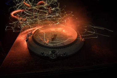 Zaman kavramı. Soyut ışıkla ahşap masada büyük klasik yuvarlak saat. Karanlık atmosfer. Yaratıcı dekorasyon. Seçici odak