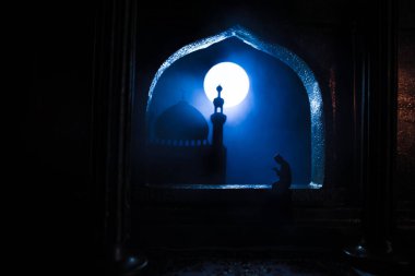 Pencere ve sütunları olan gerçekçi bir Arap iç mimarisi. Müslüman silueti pencerenin yanındaki halıda dua ediyor. Kutlama kartı, Müslüman kutsal ayı için davetiye Ramazan Kareem. Seçici odak