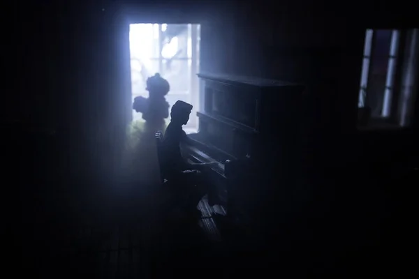 A realistic dollhouse living room with furniture and window at night. Man sitting at the old piano in dark room. Selective focus.