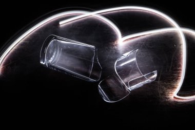 İçki, kırık cam konsepti. Ahşap masada kırık bardaklar, sisli, koyu tonlu arka plan. Seçici odak