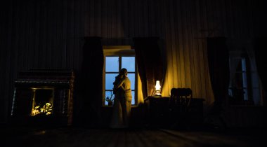 Geceleri mobilyası ve penceresi olan gerçekçi bir bebek evi oturma odası. Pencerede oturan romantik bir çift. El yapımı gerçekçi bebek eviyle sanat masası dekorasyonu. Seçici odak.