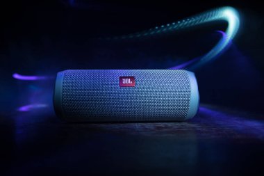 BAKU. AZERBAIJAN - 28.07.2020: JBL Flip 4 Bluetooth Hoparlörü, ahşap masaya yakın çekim, renkli ışıklar ve arka planda sis. Seçici odak