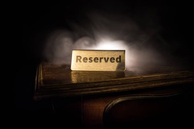 Masaya ayırtılmış tabela. Ahşap masaya bir etiket yerleştirilmiş. Karanlıkta rezervasyonu olan metal etiket. Bir restoranda rezervasyon masası. Renkli ışıklarla yaratıcı bir kavram. Seçici odak