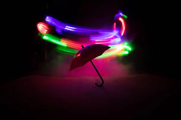 Silhouette of umbrella miniature on table with dark toned foggy background. Creative concept. Selective focus