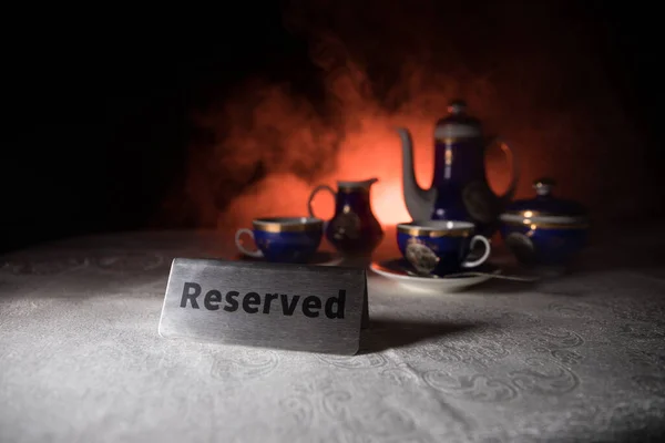 Reserved sign on the table. A tag of reservation placed on the wood table. Metal tag with reservation on dark. Reserved table in a restaurant. Creative concept with colorful lights. Selective focus