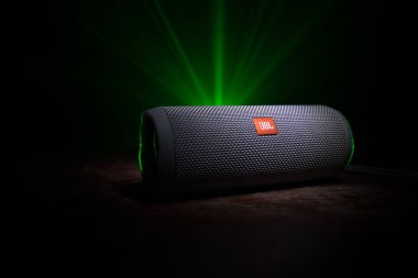BAKU. AZERBAIJAN - 28.07.2020: JBL Flip 4 Bluetooth Hoparlörü, ahşap masaya yakın çekim, renkli ışıklar ve arka planda sis. Seçici odak