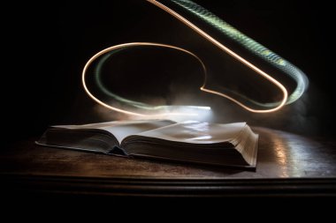 Bir yığın eski kitap. Ahşap masanın üzerinde antika bir kitap. Karanlıkta parlayan bir kitabın etrafında sihirli bir yıldırım. Seçici odak