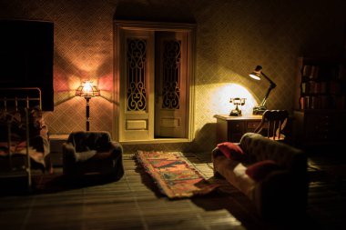 Geceleri mobilyası ve penceresi olan gerçekçi bir bebek evi oturma odası. El yapımı gerçekçi bebek eviyle sanat masası dekorasyonu. Adam karanlık odada eski tarz televizyon sallıyor. Seçici odak.