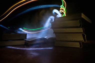 Bir yığın eski kitap. Ahşap masanın üzerinde antika bir kitap. Karanlıkta parlayan bir kitabın etrafında sihirli bir yıldırım. Seçici odak
