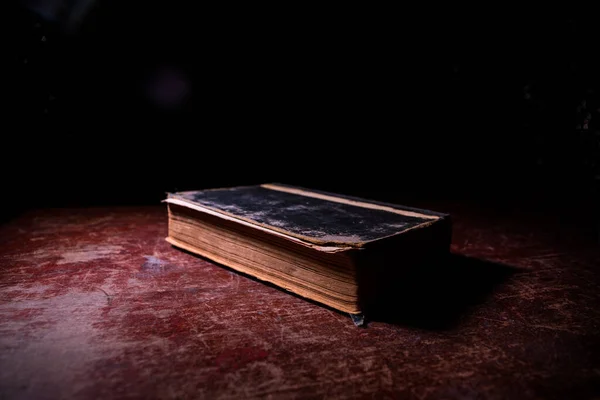 A stack of old books. Vintage book on wooden table. Magic lightning around a glowing book in the room of darkness. Selective focus